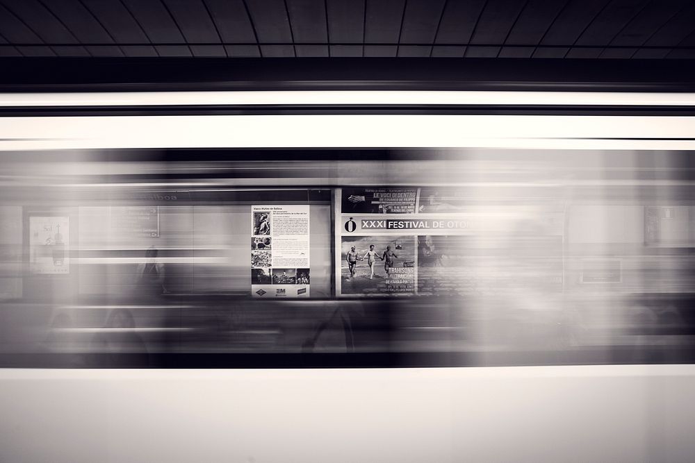 A long-exposure shot of a moving subway train and advertisement posters at the station. Original public domain image from…