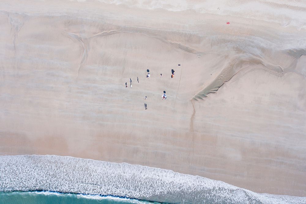An aerial view of a small group of people on a vast beach. Original public domain image from Wikimedia Commons