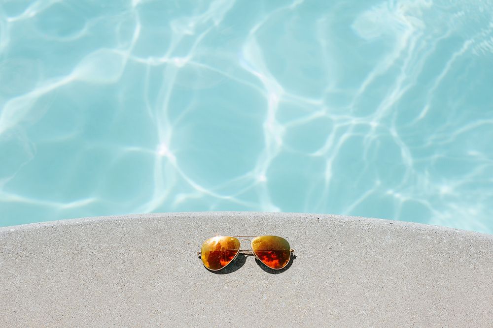 A pair of sunglasses left on a concrete ledge over clear water. Original public domain image from Wikimedia Commons