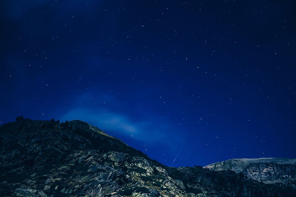 Dark blue sky speckled with stars over jagged mountain slopes. Original public domain image from Wikimedia Commons