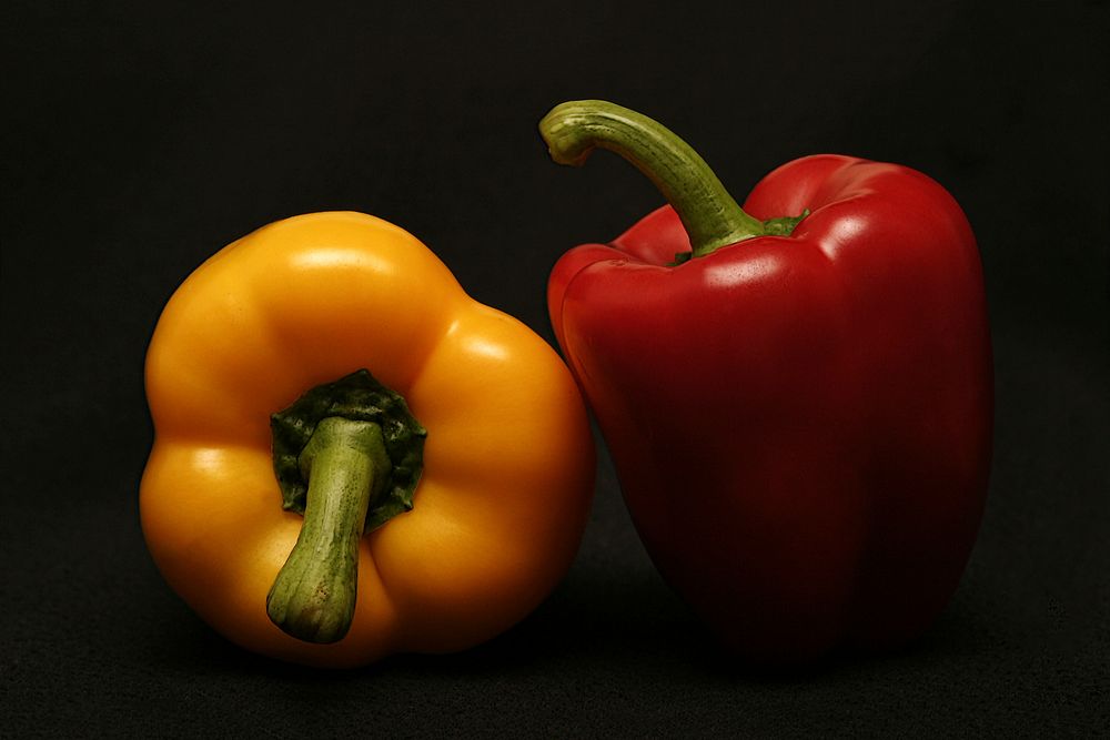 Red and yellow bell peppers in the shadows against a black background. Original public domain image from Wikimedia Commons