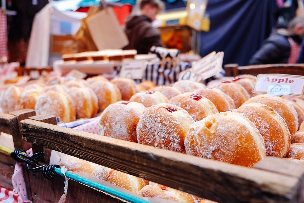 Fresh donuts with red filling on display in a market filled with people. Original public domain image from Wikimedia Commons