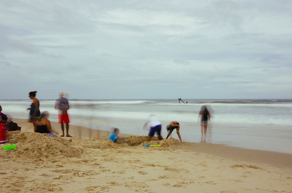 A long-exposure shot of a group of people on a beach with children digging a deep hole. Original public domain image from…