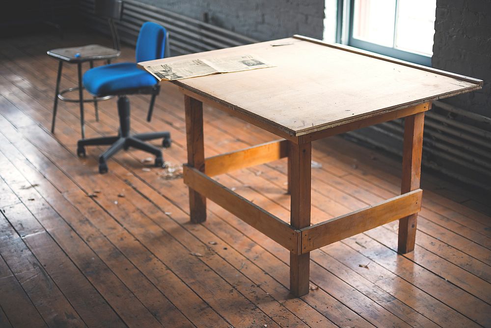 An old table near a blue office chair in a messy room. Original public domain image from Wikimedia Commons