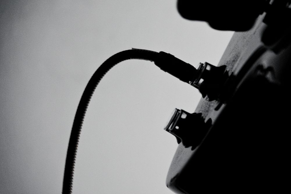 A black-and-white shot of a wire plugged in into a guitar. Original public domain image from Wikimedia Commons