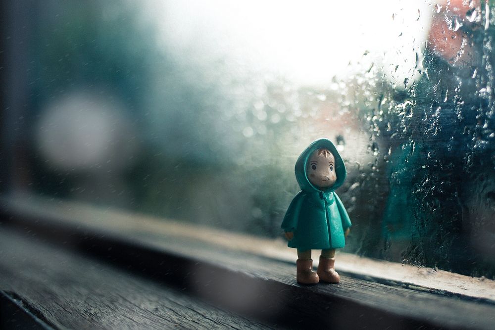 A little figure toy sitting in front of a window on a rainy day in Indonesia. Original public domain image from Wikimedia…