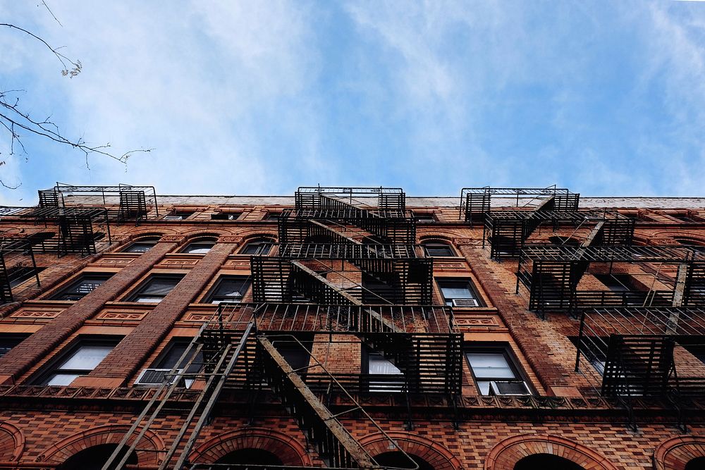 Ground view of a red brick apartment building and fire escape in New York City. Original public domain image from Wikimedia…