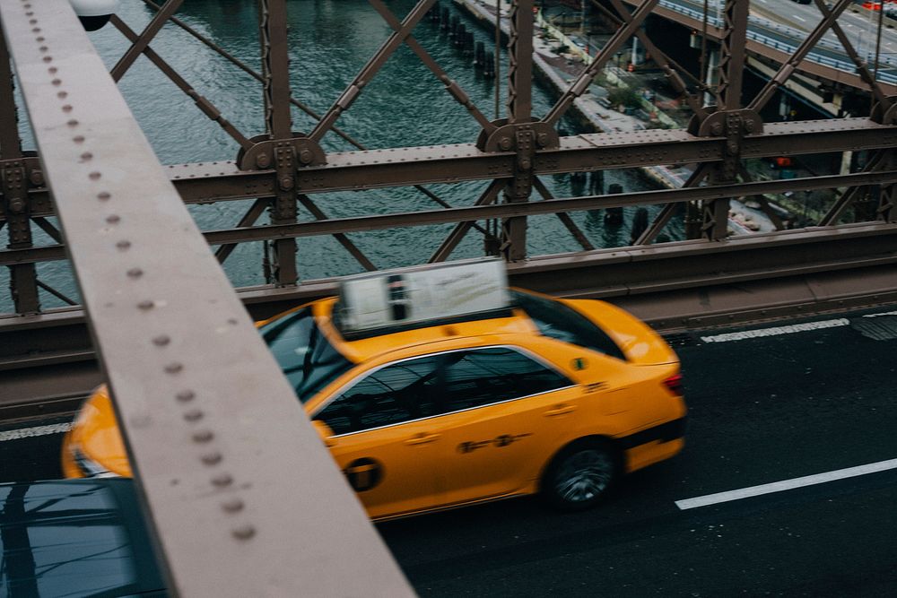 A high view of a yellow taxi cab driving on a bridge. Original public domain image from Wikimedia Commons