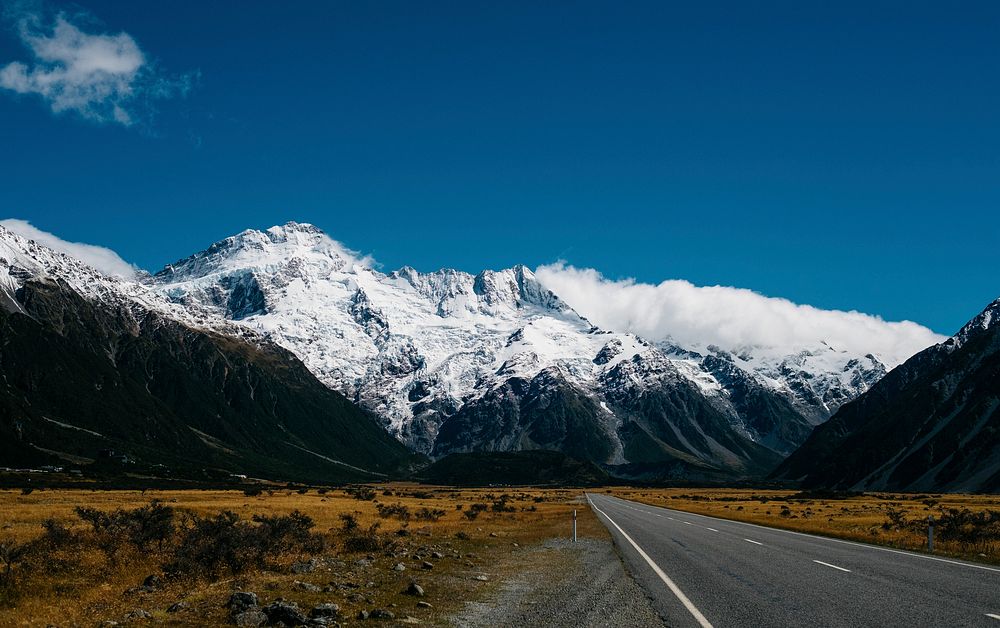 An asphalt road running towards snowy mountains under thick clouds. Original public domain image from Wikimedia Commons
