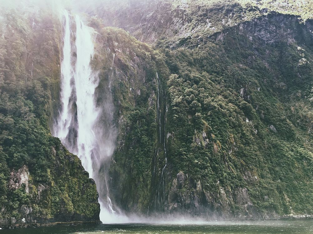 A tall waterfall pouring down from a green cliff in Milford Sound. Original public domain image from Wikimedia Commons
