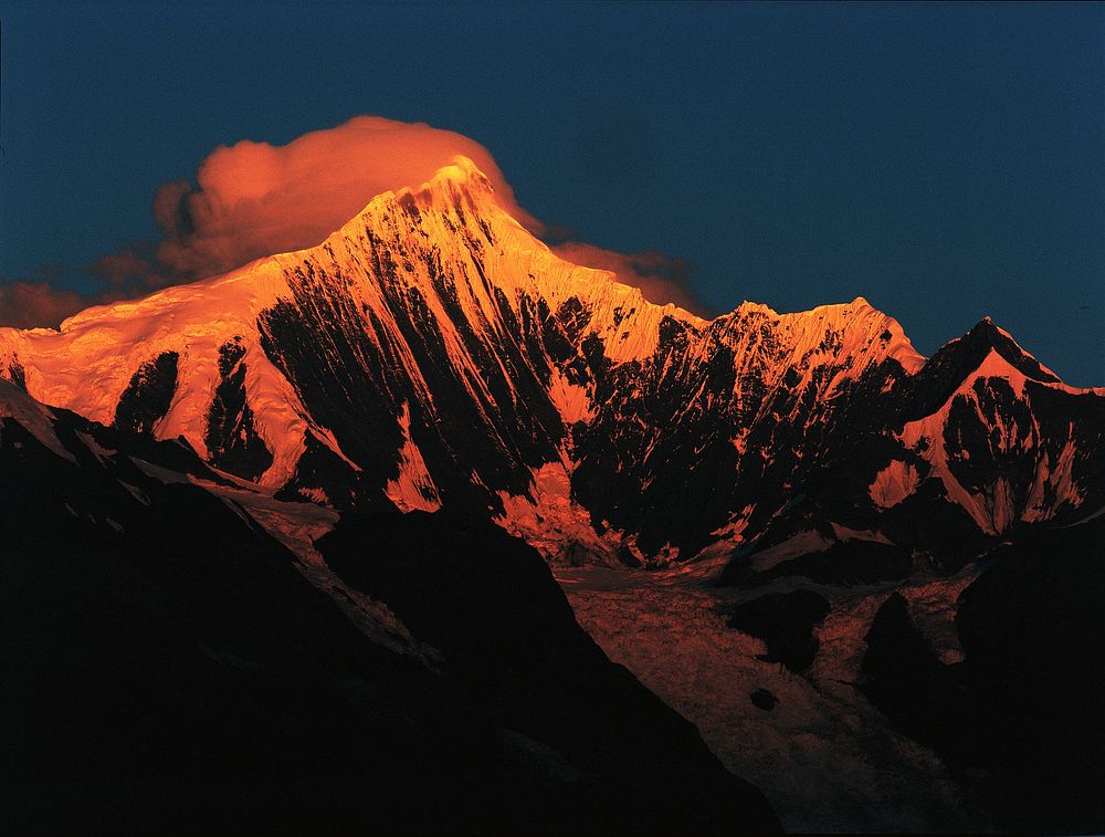 Orange sun rays illuminate a snow-capped mountain during sunrise. Original public domain image from Wikimedia Commons