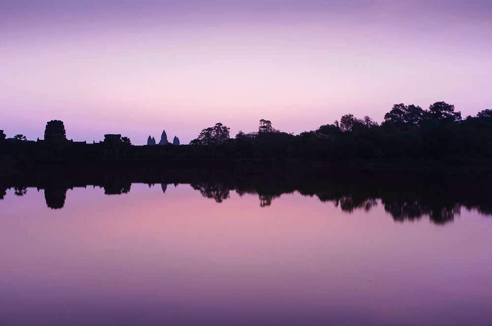 Lake shoreline is reflected in still water during a purple sunset at dusk.. Original public domain image from Wikimedia…