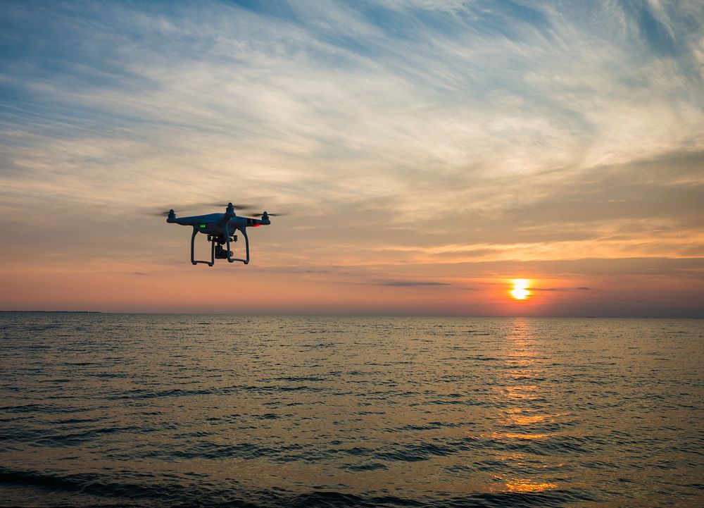 A drone flying over the sea capturing a cloudy orange sunset. Original public domain image from Wikimedia Commons