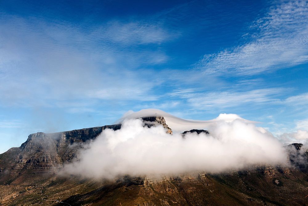 A fluffy cloud enveloping a rocky mountaintop on a bright day. Original public domain image from Wikimedia Commons