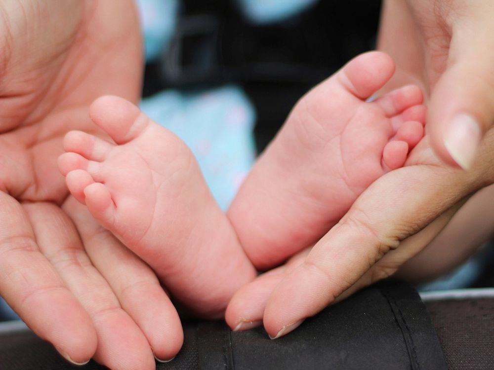 Mother's hands frame baby's feet in close-up shot. Original public domain image from Wikimedia Commons