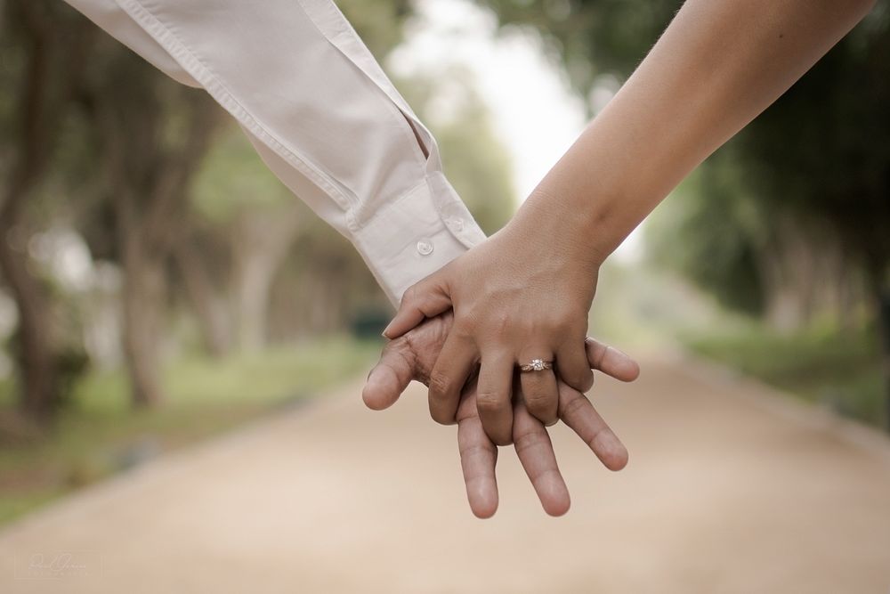 Close-up of an engaged couple holding hands outdoors. One wears a long-sleeved shirt.. Original public domain image from…