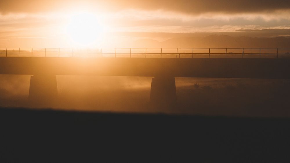 A hazy golden sunset puts a modern bridge into silhouette at Rangitata River.. Original public domain image from Wikimedia…