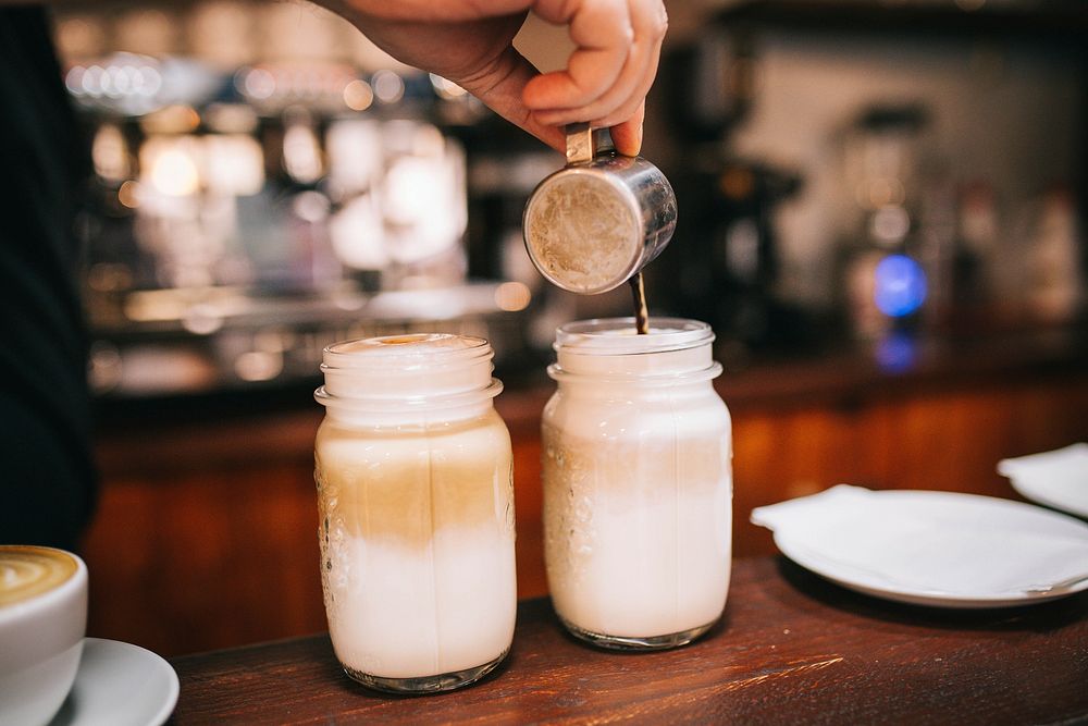 A person pouring coffee into jars with foamed milk. Original public domain image from Wikimedia Commons