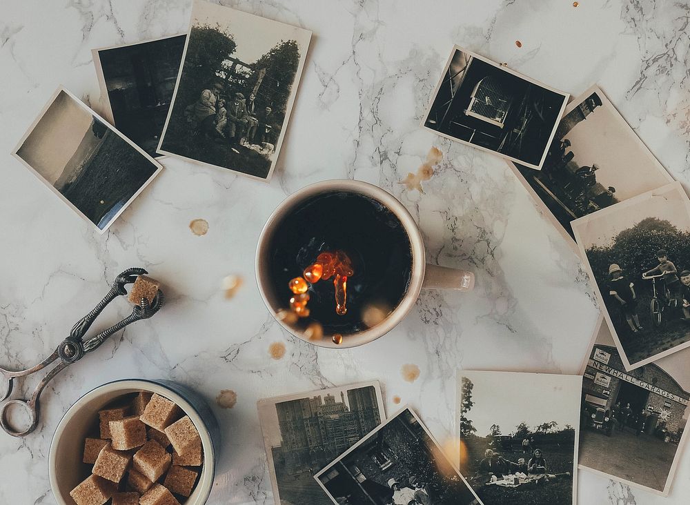 A flatlay with a cup of coffee, brown sugar cubes and black-and-white photographs. Original public domain image from…