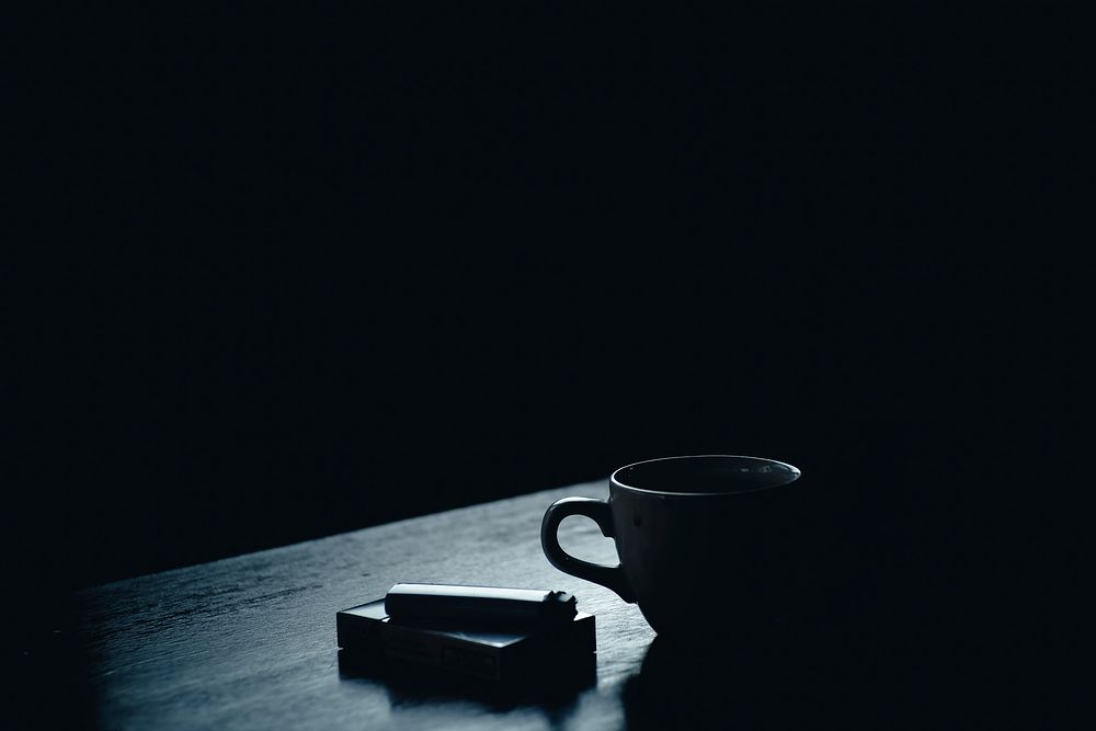 A dim shot of a pack of cigarettes and a lighter next to a teacup. Original public domain image from Wikimedia Commons