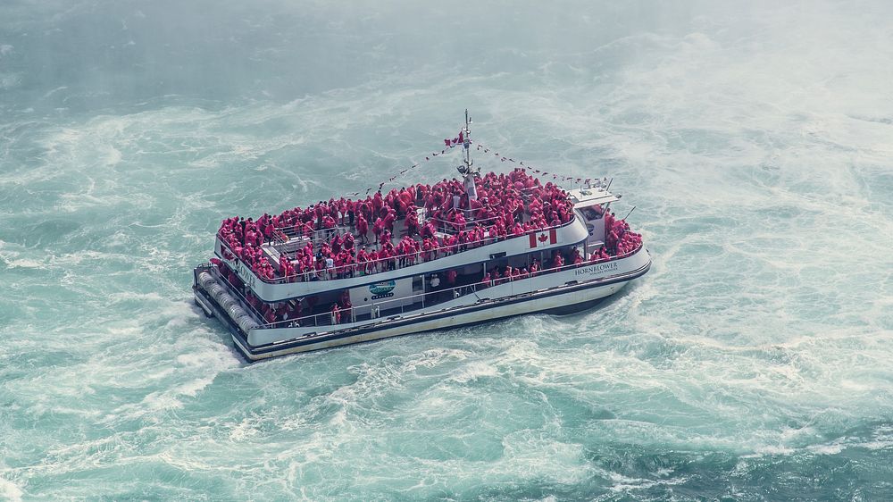 A boat full of tourists in red life jackets on the frothy water near Niagara Falls. Original public domain image from…