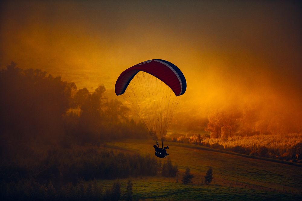 A paraglider in the air against orange-hued clouds over the countryside. Original public domain image from Wikimedia Commons