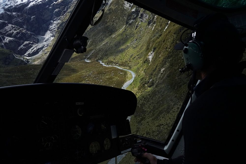 Interior shot of a person piloting a helicopter flying over a wide ravine. Original public domain image from Wikimedia…