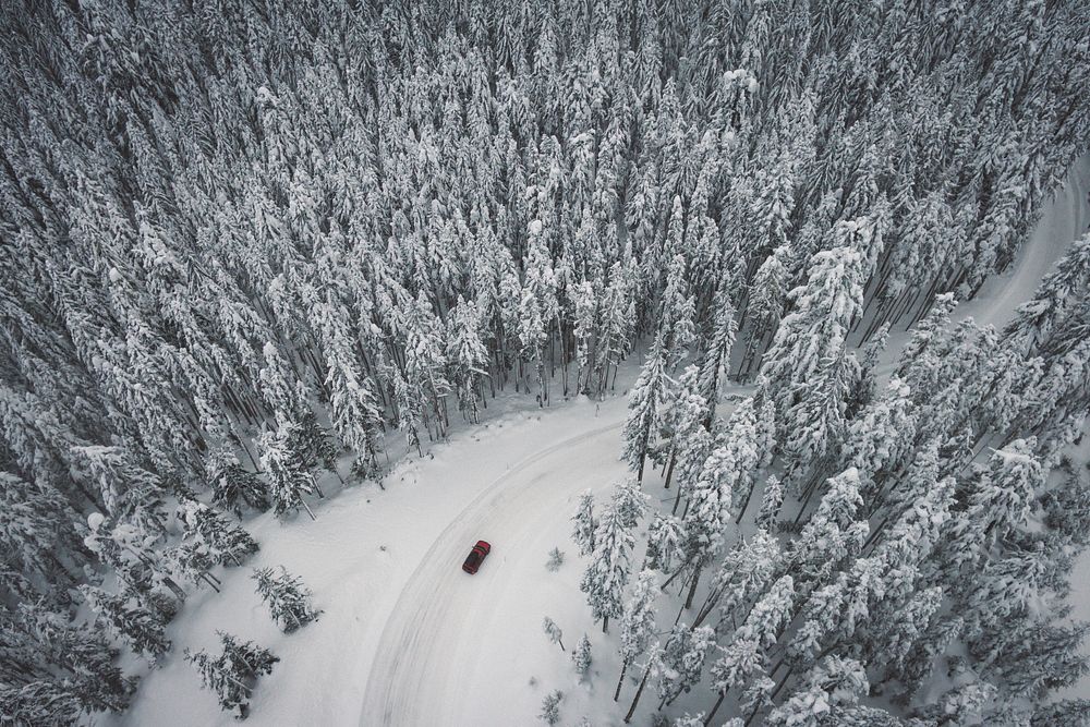 Aerial drone view of a car on a winding snow covered road through pine forest in Mount Hood National Forest. Original public…
