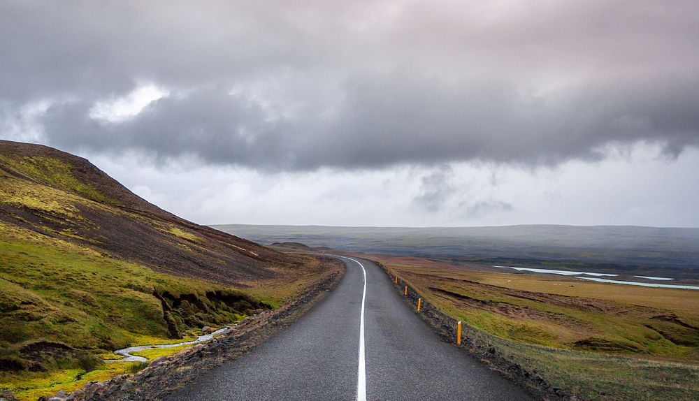 Open road leads through a rural grassy hillside on a cloudy day. Original public domain image from Wikimedia Commons