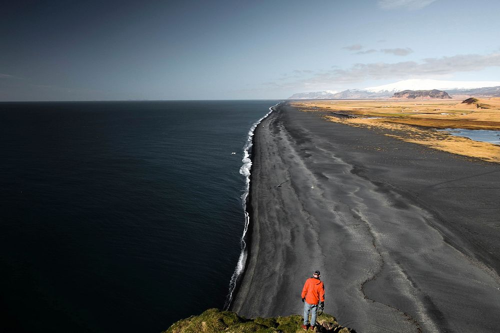 Man standing on the rock looking at the black sand beach in Vik. Original public domain image from Wikimedia Commons