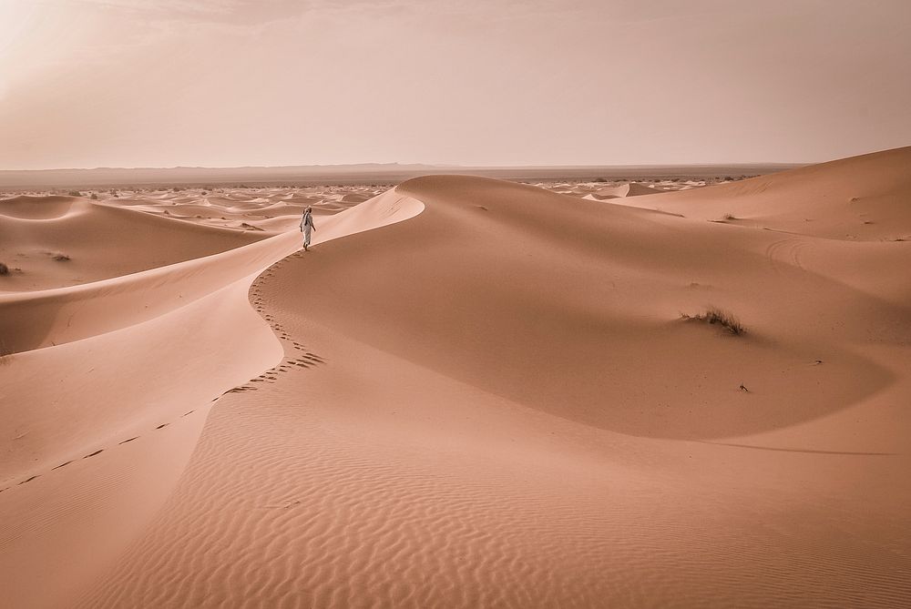 Hiker walks along a sandy ridge in the desert of Merzouga. Original public domain image from Wikimedia Commons