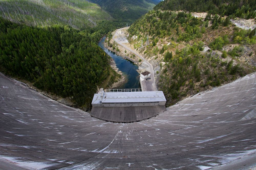 View from the top of a tall concrete dam on the river below. Original public domain image from Wikimedia Commons
