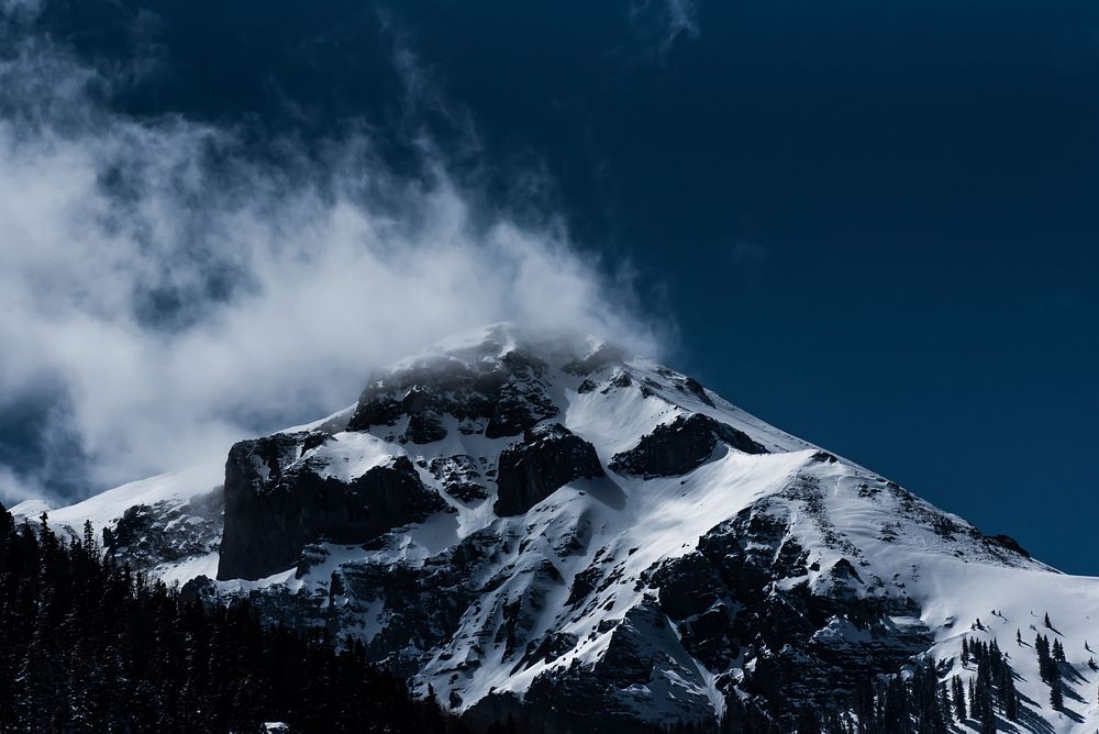 Wisps of smoke and clouds over a snowcapped mountain peak. Original public domain image from Wikimedia Commons