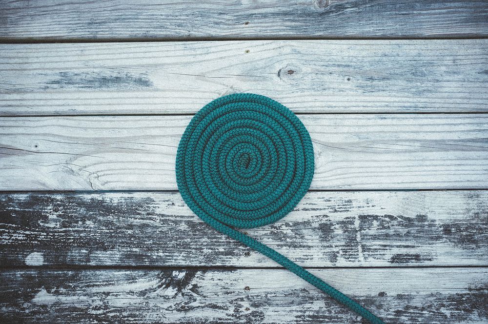 A green rope shaped like a coil on top of a wooden deck. Original public domain image from Wikimedia Commons