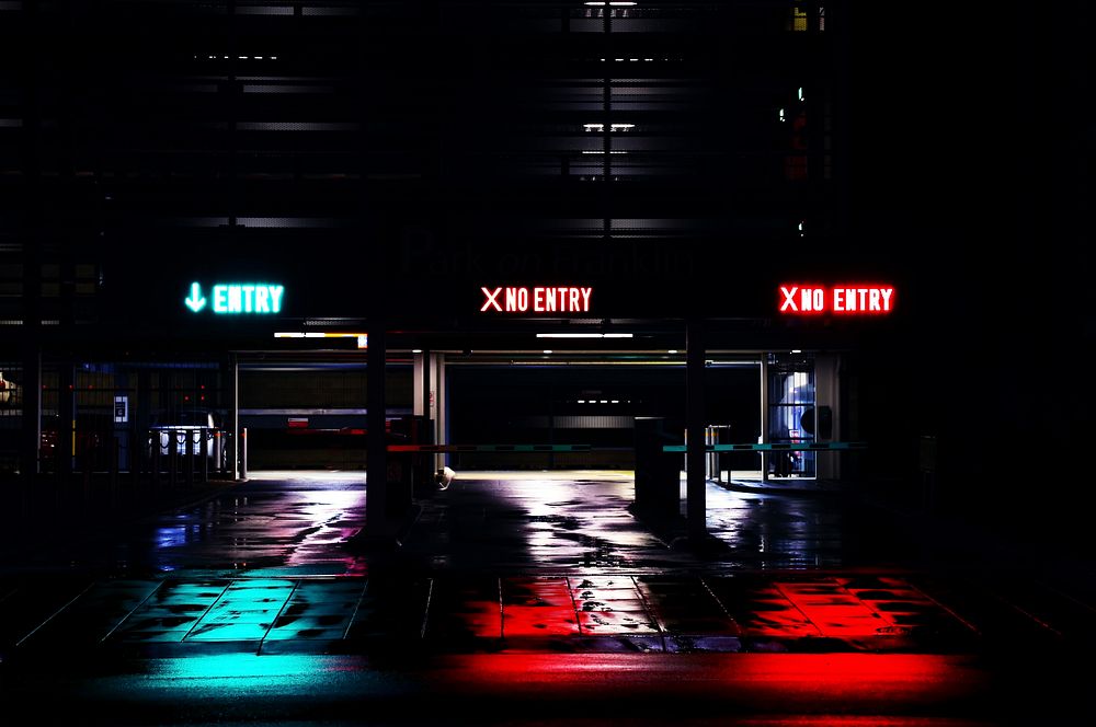 Three entrances to parking garage at night with neon signs that say Entry or No Entry. Original public domain image from…