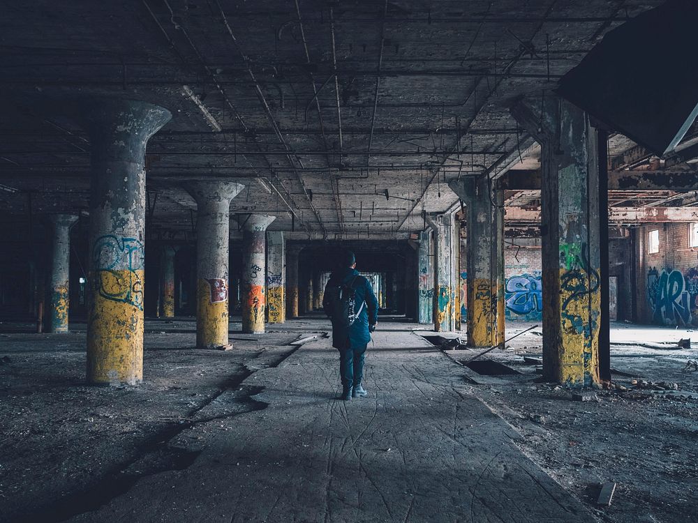 A man standing in an abandoned parking garage that's filled with graffiti in Detroit. Original public domain image from…