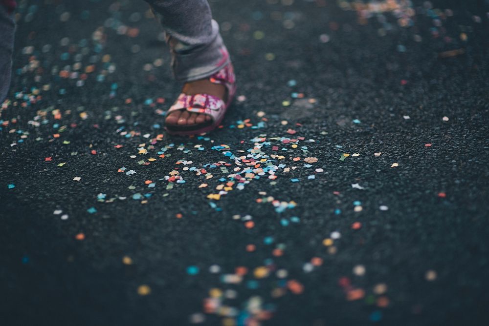 A child's foot in a pink sandal, on the ground, among confetti.. Original public domain image from Wikimedia Commons