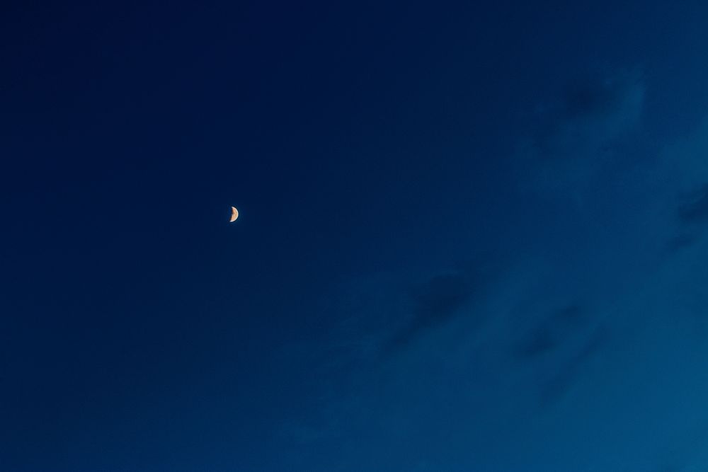 Crescent moon seen near fluffy clouds on an inky blue sky. Original public domain image from Wikimedia Commons