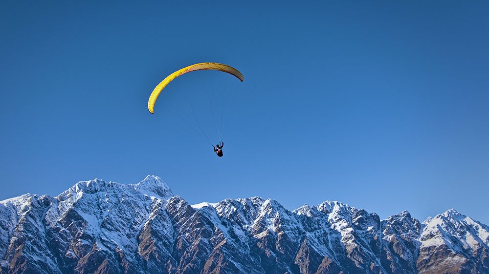 A paraglider soaring over snowy mountains. Original public domain image from Wikimedia Commons