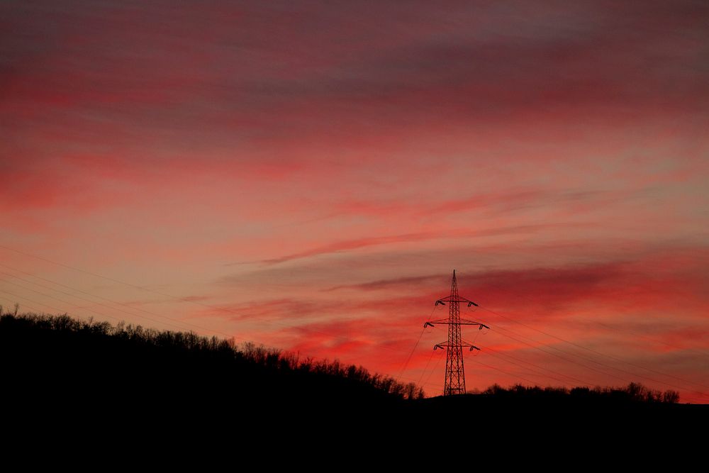 A transmission tower among trees under a red sky at dusk. Original public domain image from Wikimedia Commons