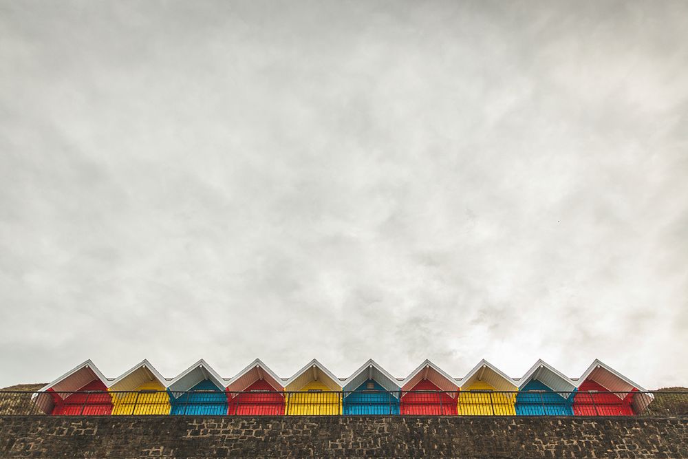 Red, yellow, and blue colored huts in line on a stone wall in Whitby. Original public domain image from Wikimedia Commons