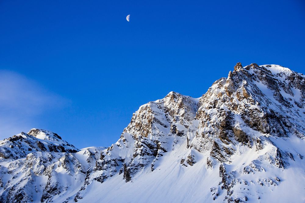 Half moon rises over the snow covered mountains in France. Original public domain image from Wikimedia Commons