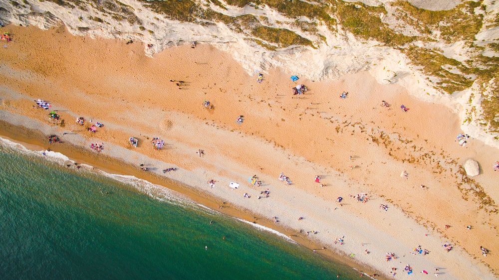 Drone aerial view of a crowded sand beach coastline at Durdle Door. Original public domain image from Wikimedia Commons