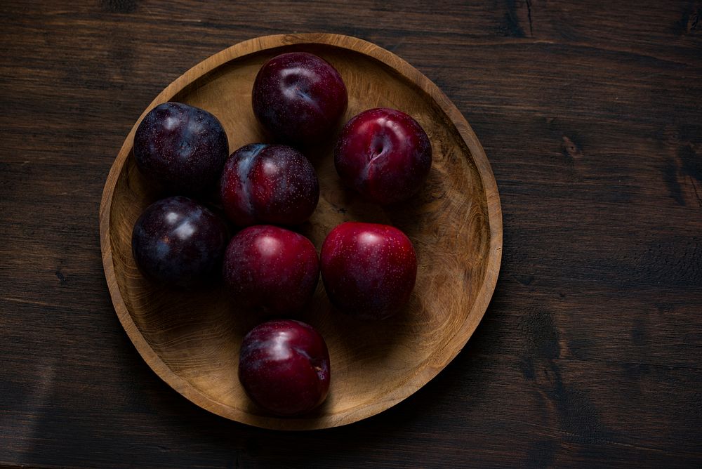 Wooden bowl of fresh plums in the kitchen ready to eat. Original public domain image from Wikimedia Commons