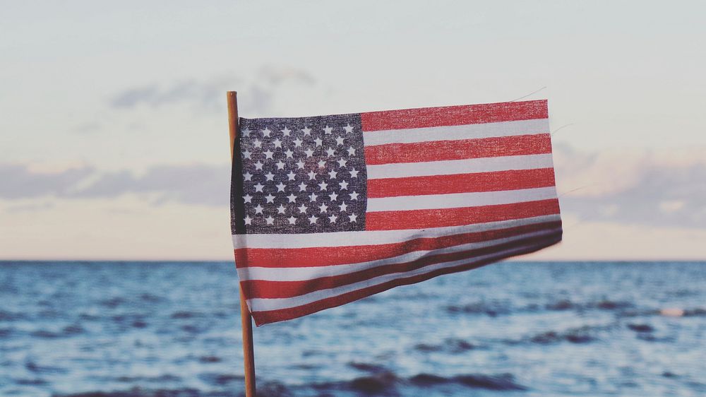 The macro view of the flag of the USA waving as the wind blows with a sea behind it.. Original public domain image from…