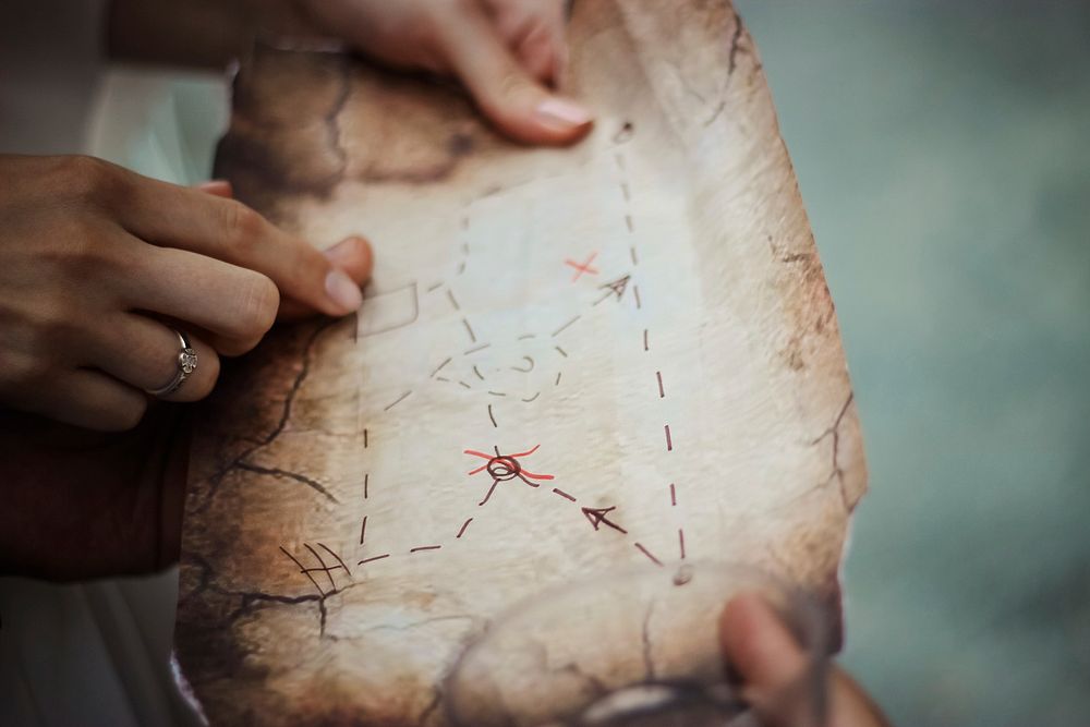 Two people holding up an old map with directions and X marks drawn with a marker. Original public domain image from…