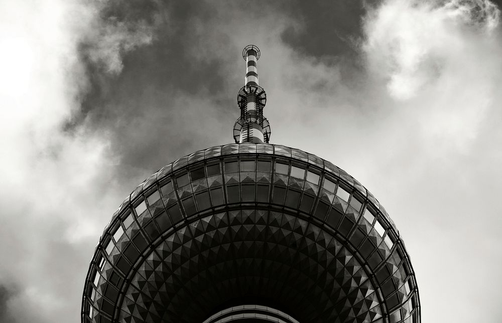 Black and white shot of modern tower from below with spire and clouds. Original public domain image from Wikimedia Commons