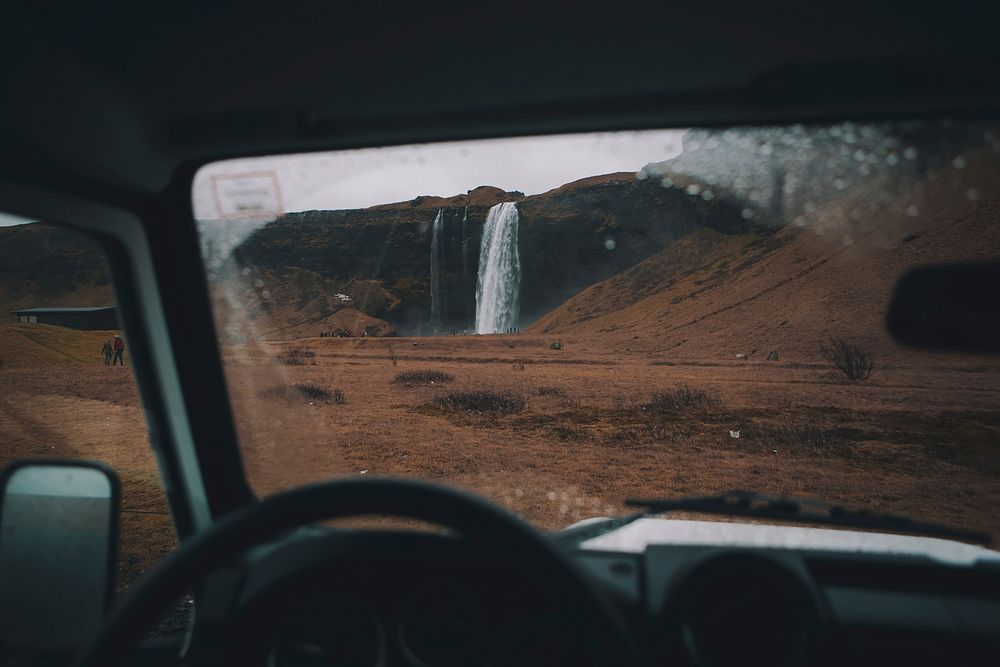 A view through a windshield on a waterfall surrounded by tourists in cold plains. Original public domain image from…