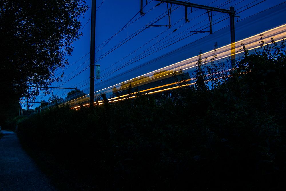 A blurred moving train on a railroad in an early night sky in Jette. Original public domain image from Wikimedia Commons