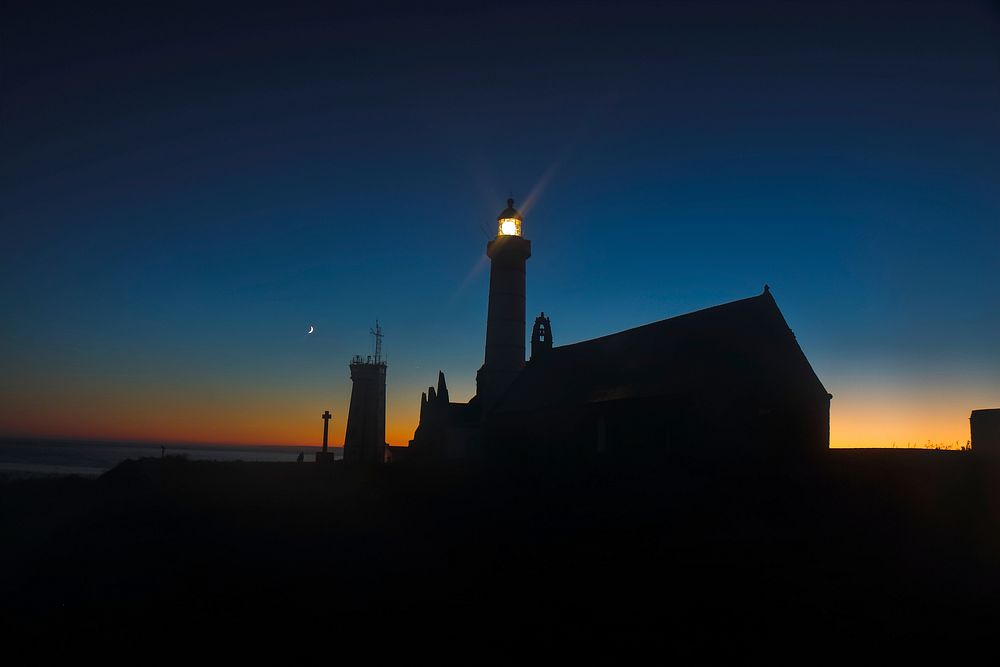The lighthouse next to the abbey at Pointe de Saint-Mathieu shines against the illuminated sky.. Original public domain…